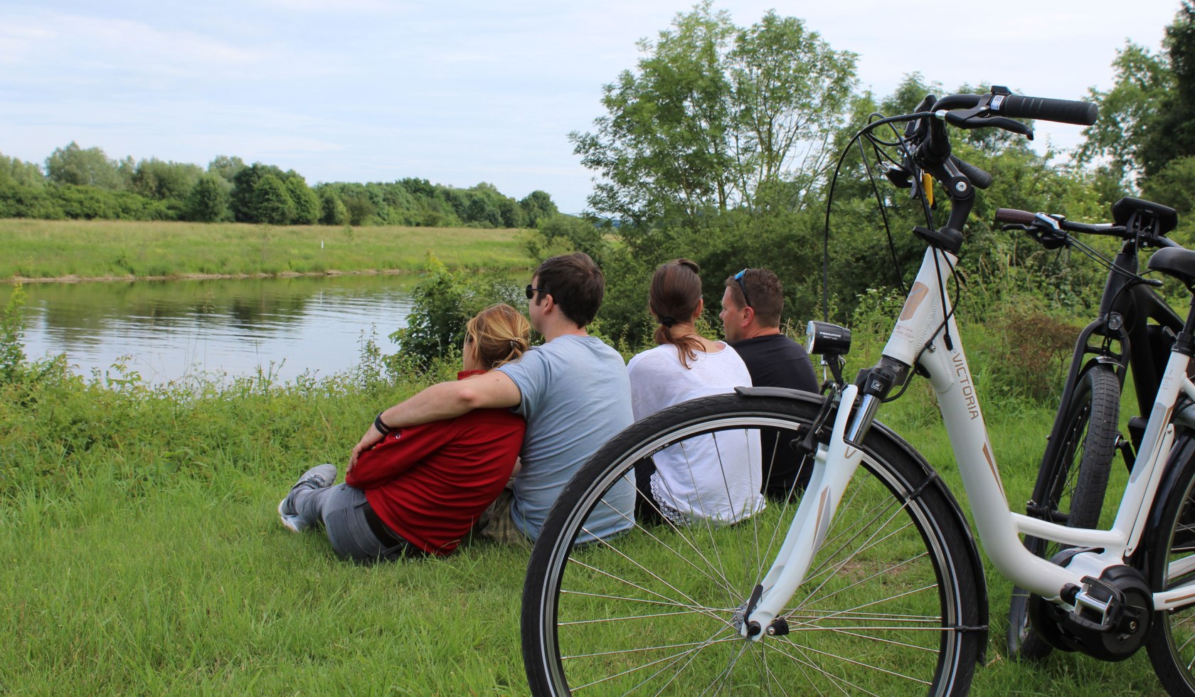 Vier Radfahrer sitzen im Gras und pausieren am Weserufer, © Mittelweser Touristik GmbH