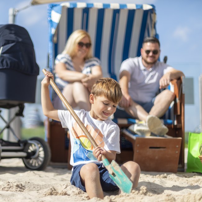 Eltern sitzen im Strandkorb und kleiner Junge gräbt im Sand, © TourismusMarketing Niedersachsen GmbH