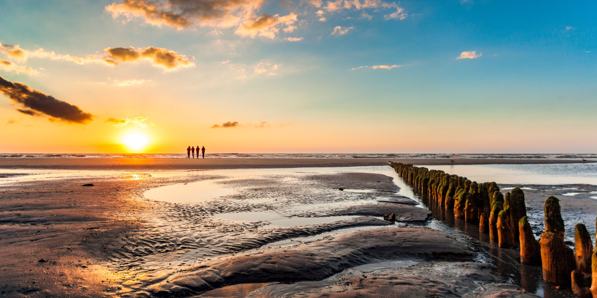 Drei Personen stehen am Nordstrand von Norderney und beobachten den Sonnenuntergang, © TMN/Janis Meyer 