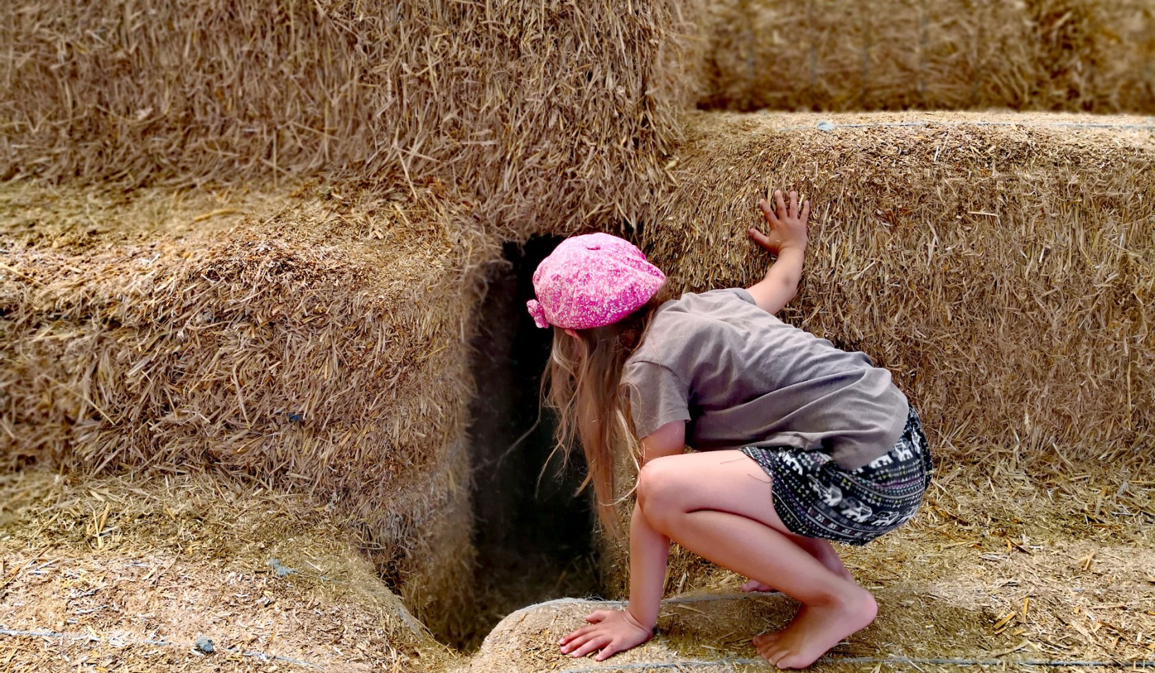 Ein Mädchen erkundet eine Höhle aus übereinandergestapelten Strohballen., © Spielplatz am Alfsee