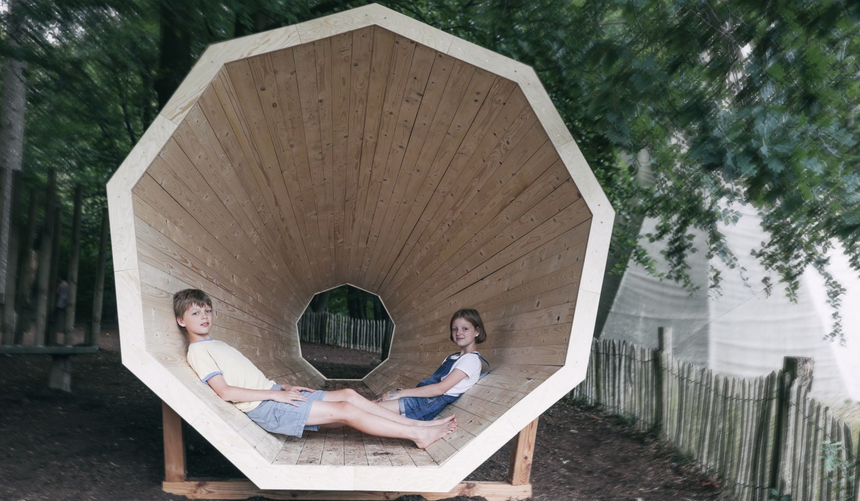 Zwei Kinder sitzen im sogenannten Waldmegaphone, einem tunnelartigen Holzbau, © Barfußpark Lüneburger Heide / Karsten Eichhorn