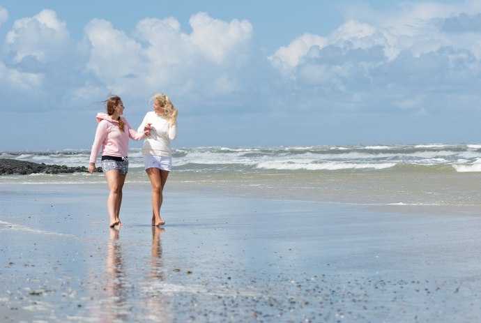 Zwei Frauen gehen mit den Füßen im Wasser am Strand entlang, © Kurverwaltung Wangerooge / Kees van Surksum
